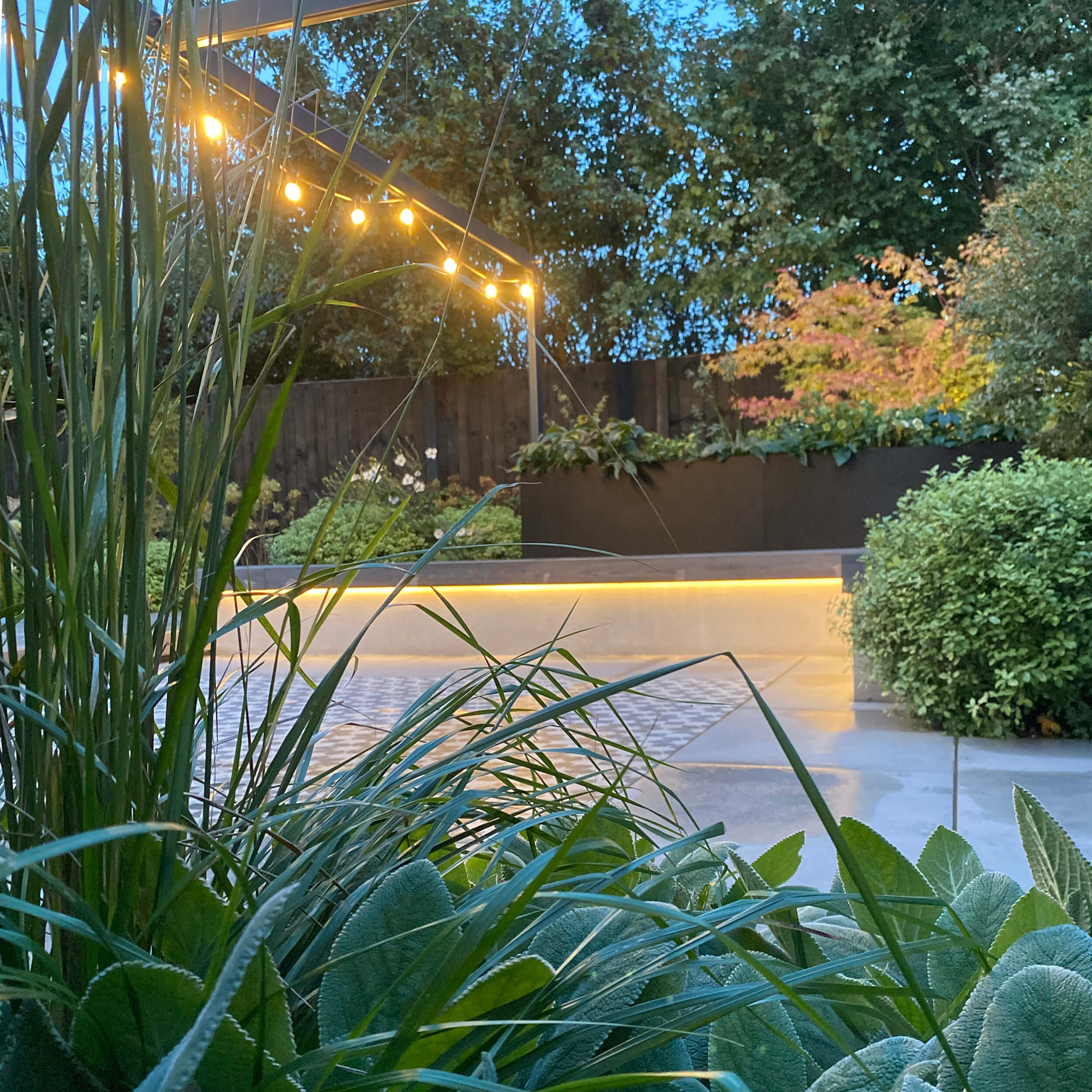 Subtle led lighting strips highlight the bespoke bench below festoon lights on the pergola