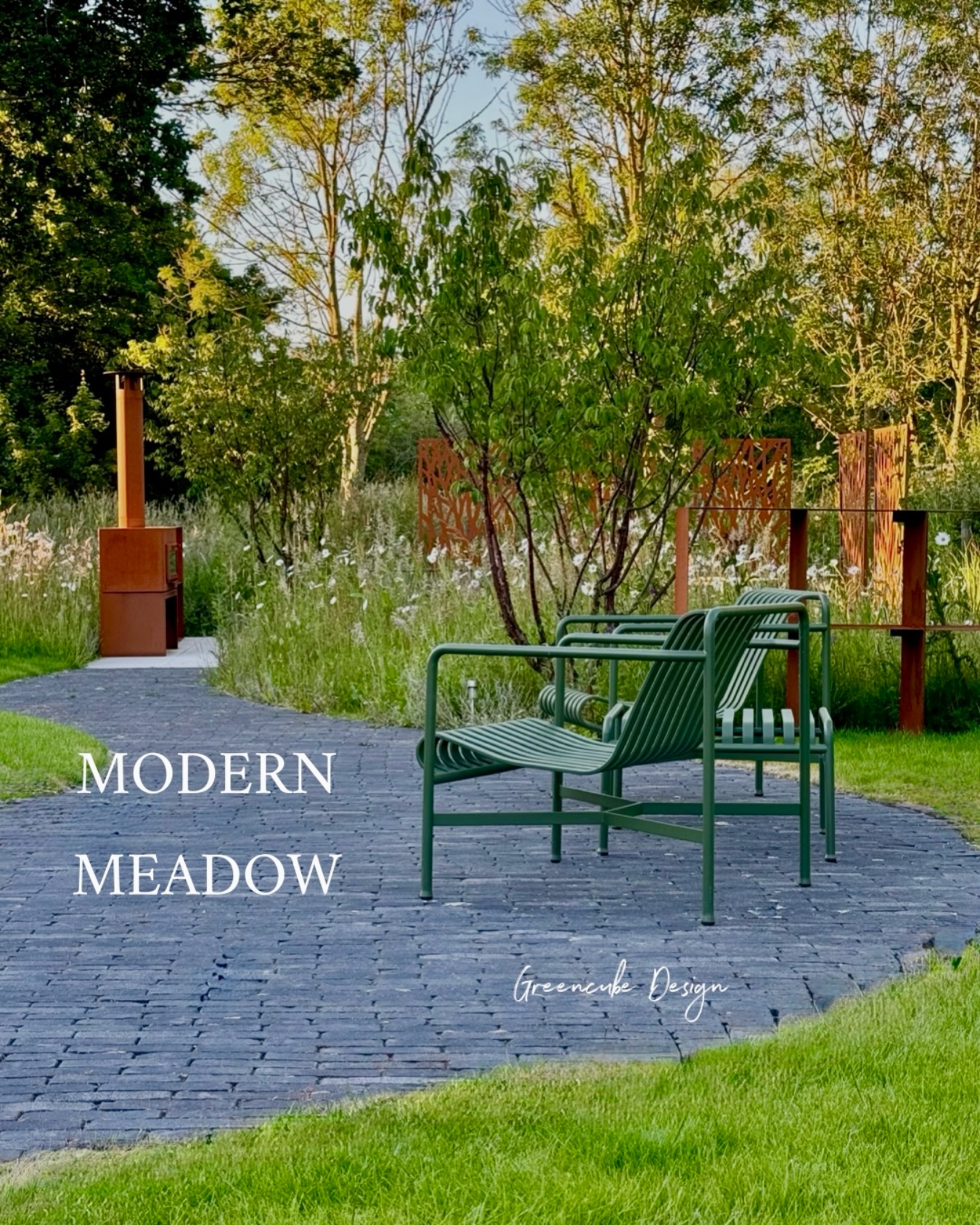 Modern garden seating area with green metal benches on a brick path, surrounded by trees and tall grasses in a meadow setting.”] ,